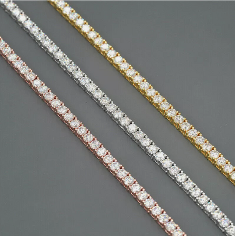 Three diamond tennis bracelets in gold, rose gold, and silver on a gray background
